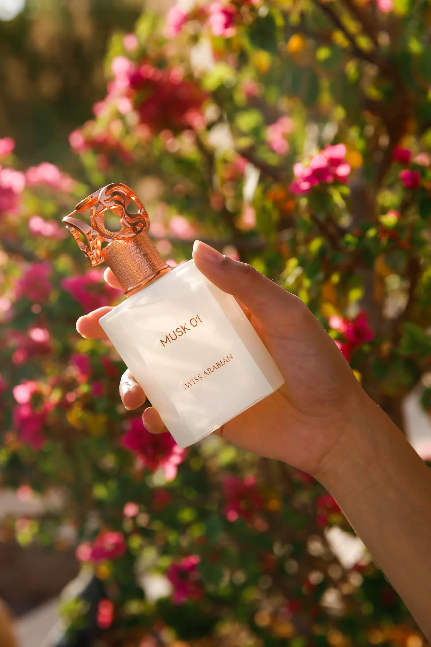 Una mano sostiene Musk 01 entre flores bajo luz natural